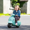 Petite fille souriante en veste en jean roulant sur la Mini Vespa électrique vert d'eau dans une allée